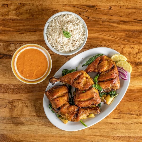Grilled chicken quarters with lemon, red onion, and greens, served with rice and a side sauce.