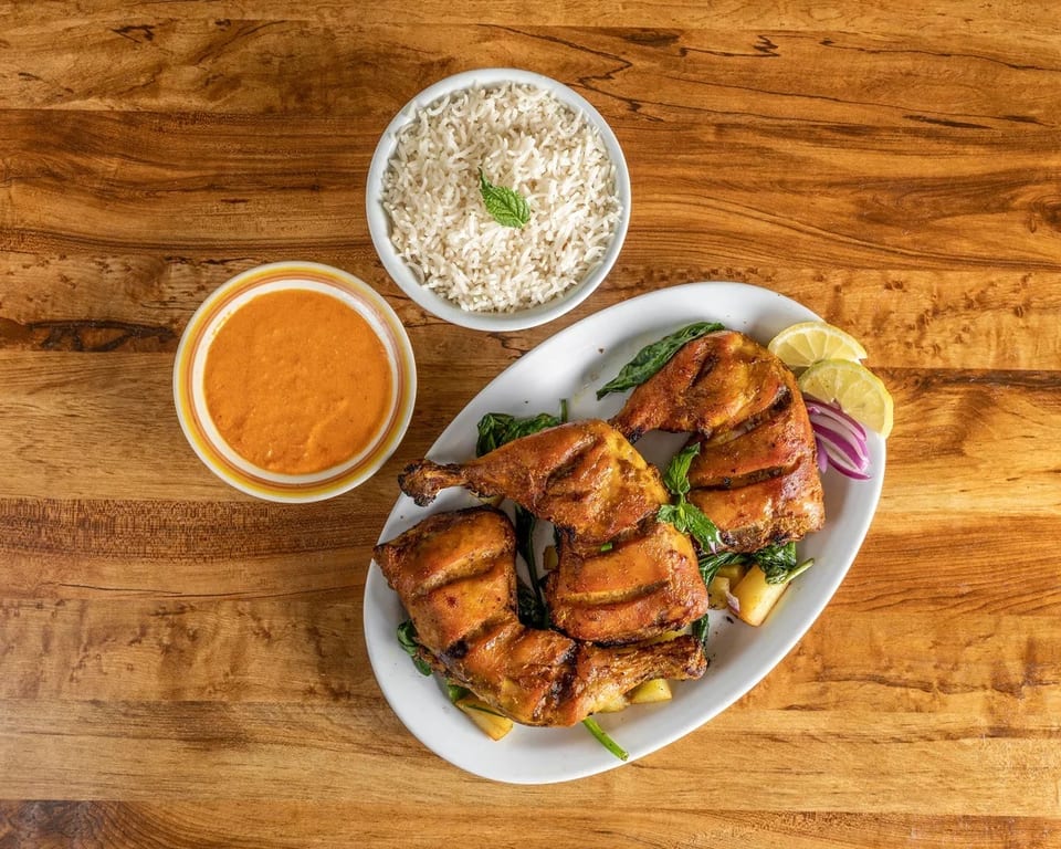 Grilled chicken quarters with lemon, red onion, and greens, served with rice and a side sauce.