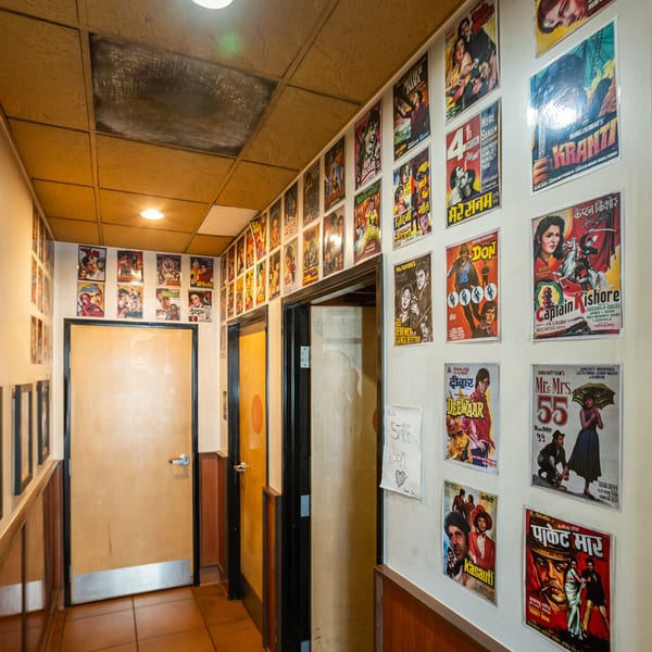 A hallway with light brown doors and walls covered in colorful vintage Bollywood movie posters.