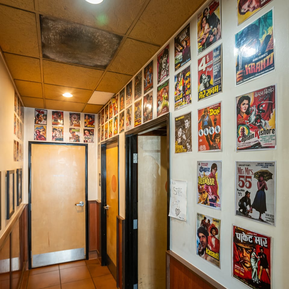 A hallway with light brown doors and walls covered in colorful vintage Bollywood movie posters.