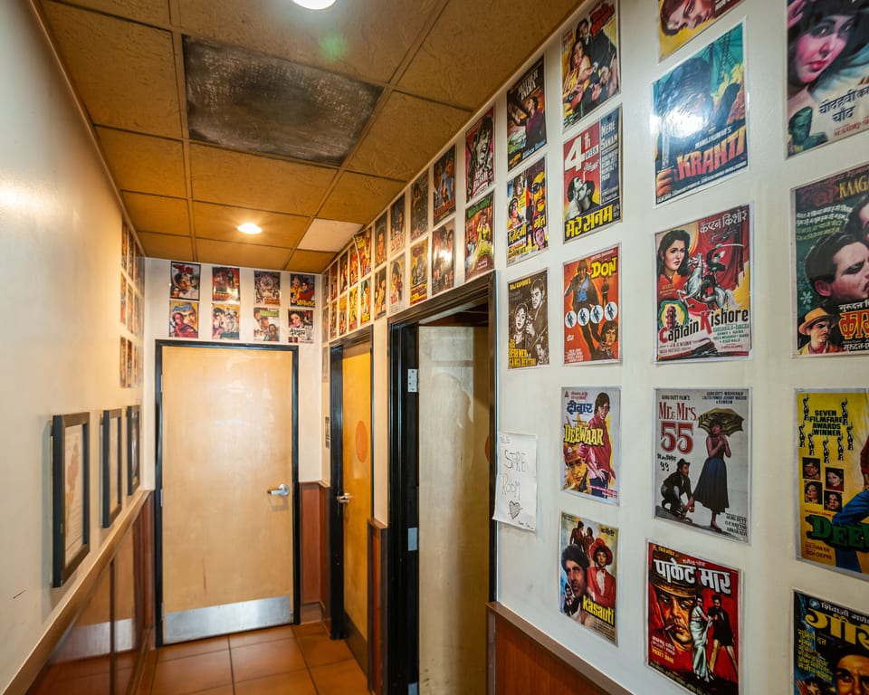 A hallway with light brown doors and walls covered in colorful vintage Bollywood movie posters.