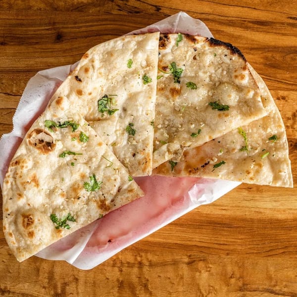 Garlic naan bread with cilantro, served in a paper-lined basket on a wooden table.