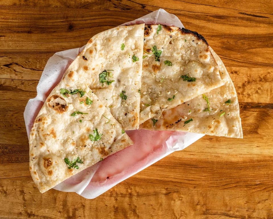 Garlic naan bread with cilantro, served in a paper-lined basket on a wooden table.