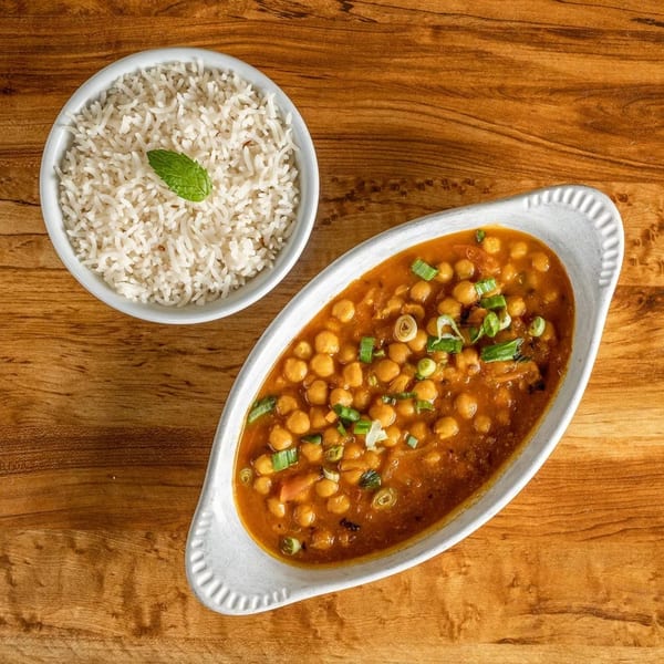 Chana Masala with chickpeas and green onions in a white dish, served with white rice and a mint leaf.