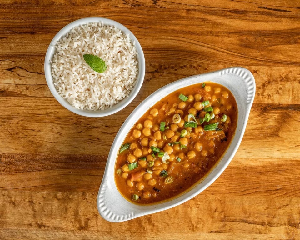 Chana Masala with chickpeas and green onions in a white dish, served with white rice and a mint leaf.