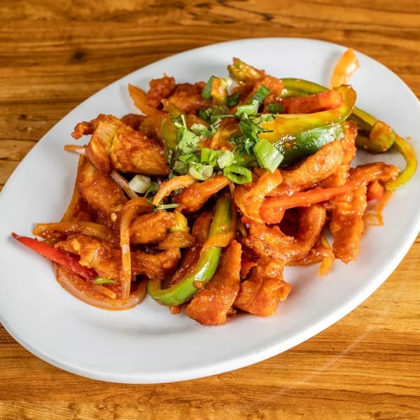 Crispy chili chicken with bell peppers, onions, and green onions on a white plate.