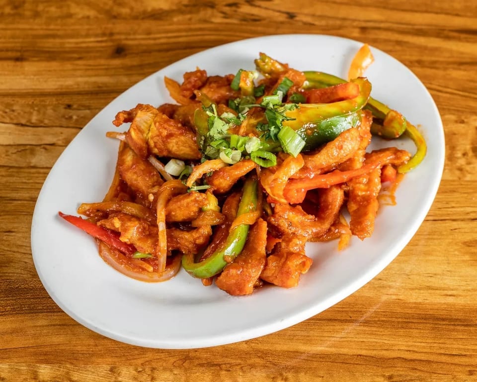 Crispy chili chicken with bell peppers, onions, and green onions on a white plate.