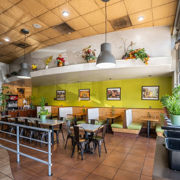 Restaurant interior with lime green walls, wooden booths, tables, and a beverage station.