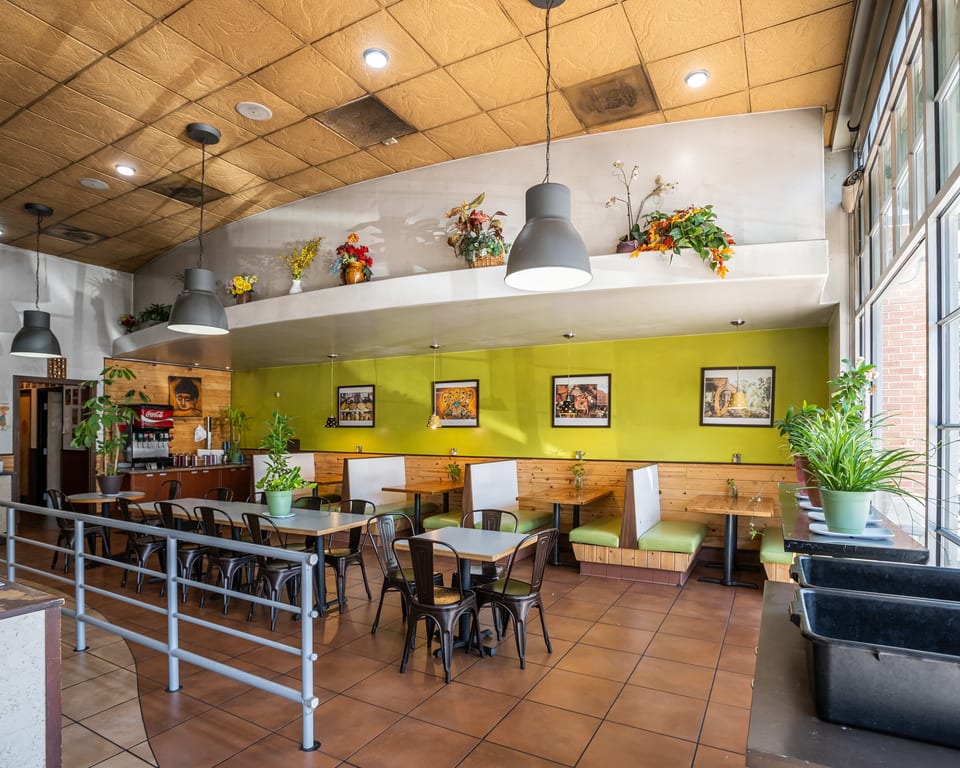 Restaurant interior with lime green walls, wooden booths, tables, and a beverage station.