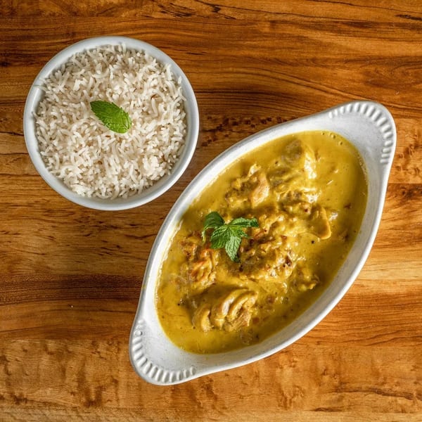 Chicken curry with rice, garnished with mint, on a wooden table.
