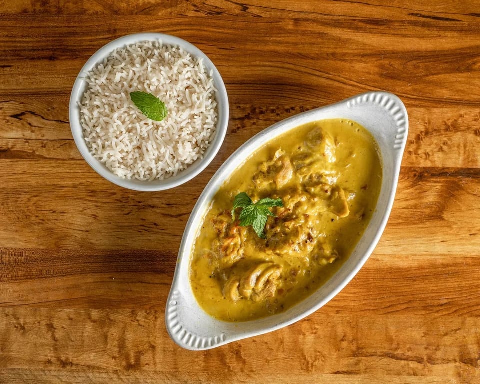Chicken curry with rice, garnished with mint, on a wooden table.