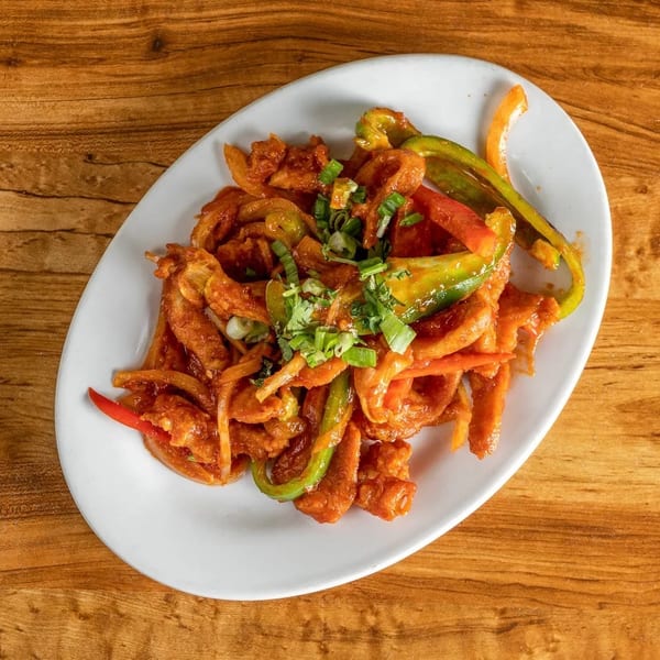 Chili chicken with bell peppers and onions, garnished with green onions, on a white oval plate.
