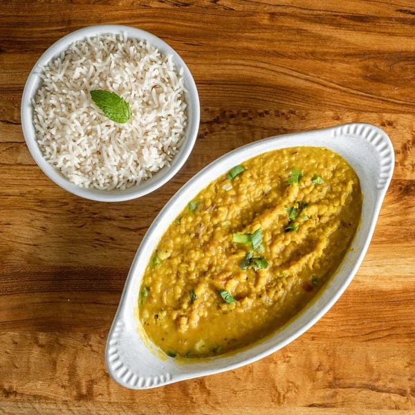 A bowl of white rice with a mint leaf and a dish of yellow lentil curry on a wooden table.