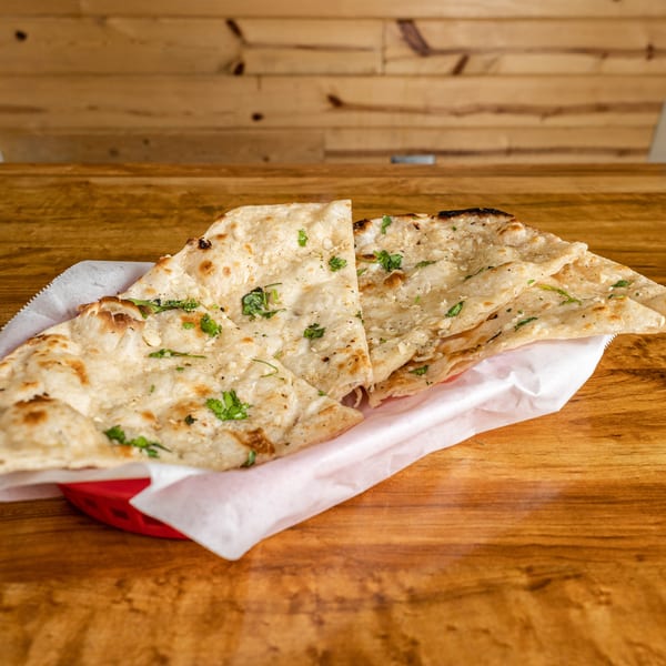 Garlic naan bread, garnished with cilantro, served in a red basket on a wooden table.