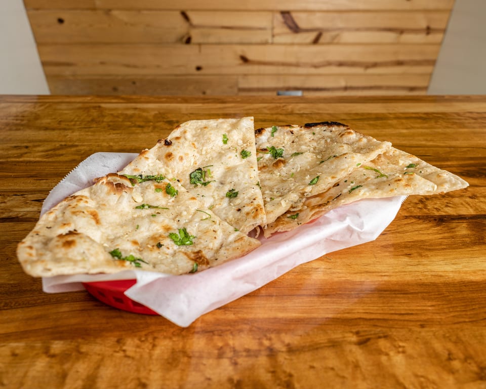 Garlic naan bread, garnished with cilantro, served in a red basket on a wooden table.