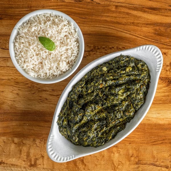 Overhead view of a white bowl of rice with a mint leaf and a white dish of green stew.