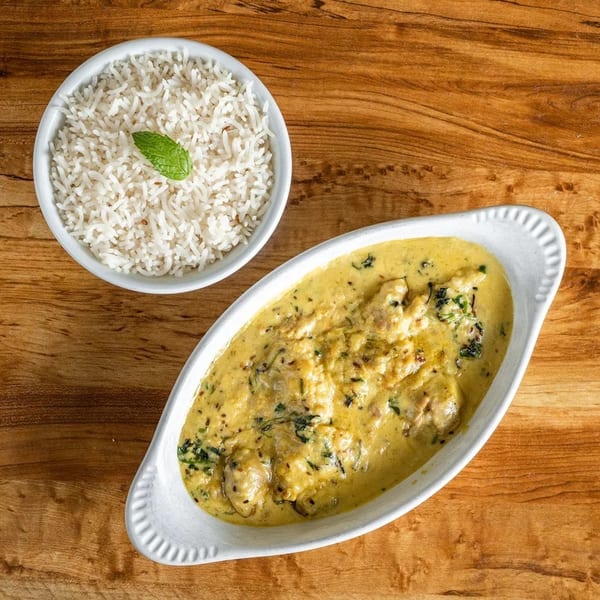 Creamy yellow curry with chicken and herbs in a white dish, served with a bowl of white rice.