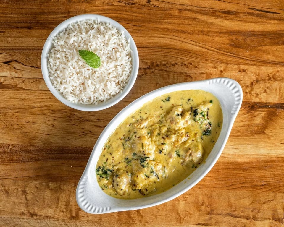 Creamy yellow curry with chicken and herbs in a white dish, served with a bowl of white rice.
